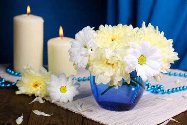 Beautiful chrysanthemum flowers in vase on table on dark blue background Royalty Free Stock Images