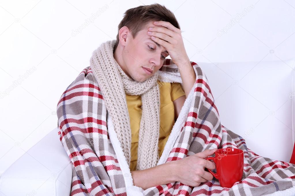 Guy wrapped in plaid lies on sofa on white background