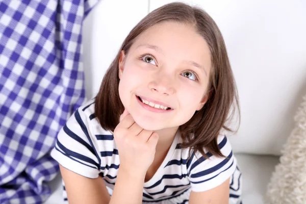 Beautiful little girl sitting on sofa, on home interior background — Stock Photo, Image