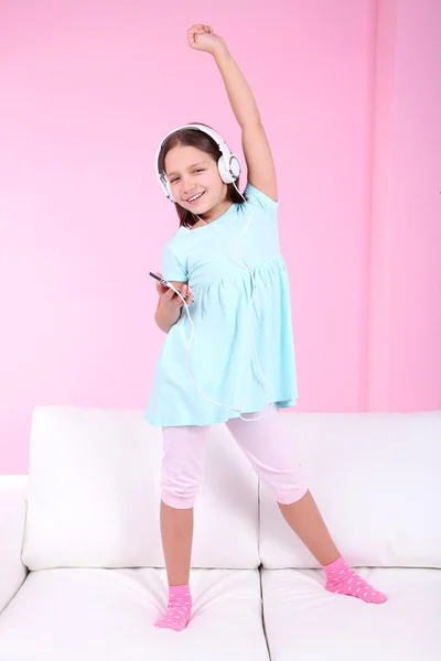 Beautiful little girl listening to music and dancing on sofa and listening to music, on home interior background — Stock Photo, Image