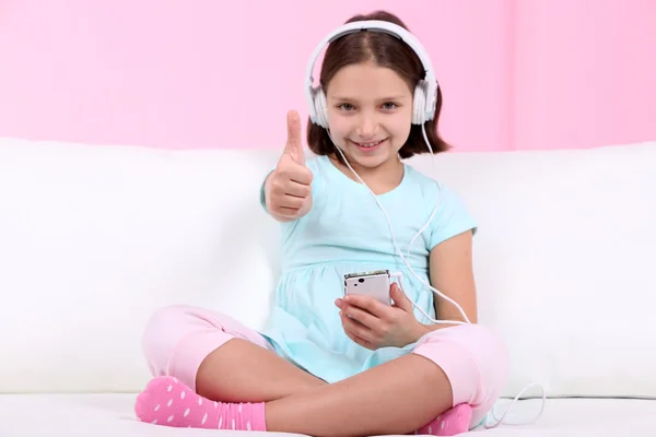 Hermosa niña sentada en el sofá y escuchando música, en el fondo interior de casa —  Fotos de Stock