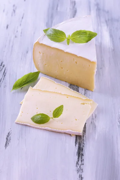 Tasty Camembert cheese with basil, on wooden table — Stock Photo, Image