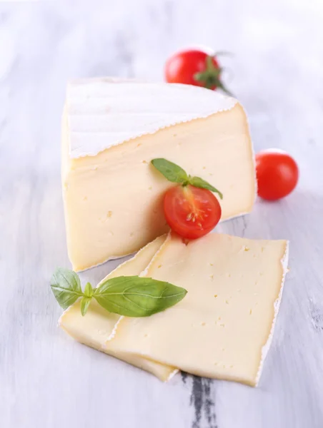 Tasty Camembert cheese with tomato and basil, on wooden table — Stock Photo, Image