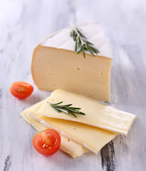 Tasty Camembert cheese with tomato and rosemary, on wooden table — Stock Photo, Image