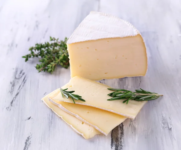 Tasty Camembert cheese with rosemary and thyme, on wooden table — Stock Photo, Image