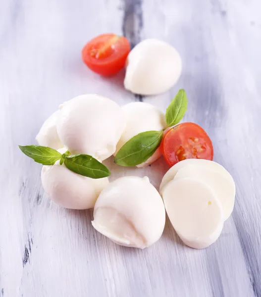 Tasty mozzarella cheese with basil and tomatoes, on wooden table — Stock Photo, Image