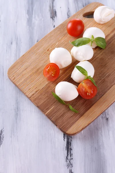 Smakelijke mozzarella kaas met basilicum en tomaten, op houten tafel — Stockfoto