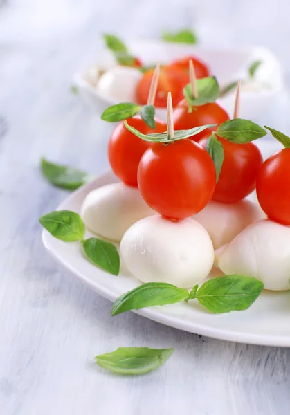 Tasty mozzarella cheese with basil and tomatoes on plate, on wooden table — Stock Photo, Image