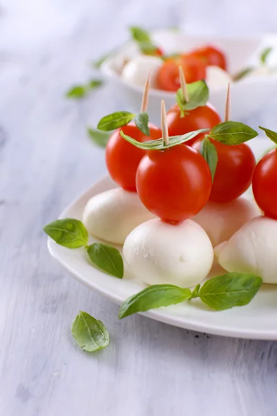 Schmackhafter Mozzarella-Käse mit Basilikum und Tomaten auf Teller, auf Holztisch — Stockfoto