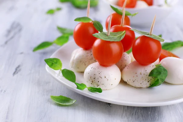 Sabroso queso mozzarella con albahaca y tomates en plato, sobre mesa de madera —  Fotos de Stock