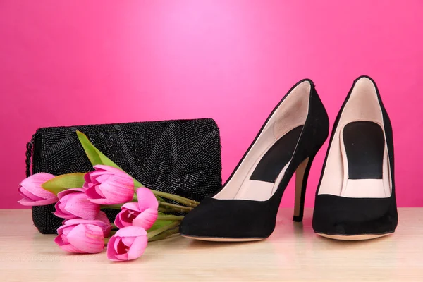 Beautiful black female shoes, bag and flowers on pink background — Stock Photo, Image