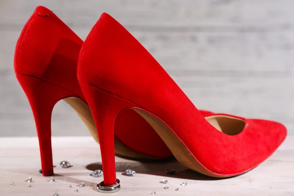 Ahşap arka plan üzerinde kırmızı kadın ayakkabı topuğu üzerinde güzel alyans — Stok fotoğraf