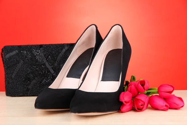 Mooie zwarte vrouwelijke schoenen, tas en bloemen op rode achtergrond — Stockfoto