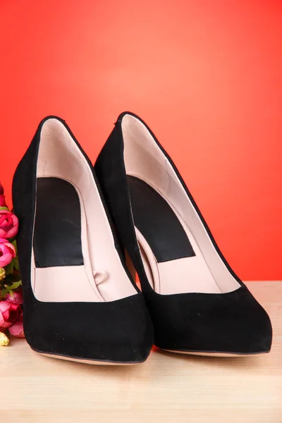 Hermosos zapatos femeninos negros y flores sobre fondo rojo — Foto de Stock