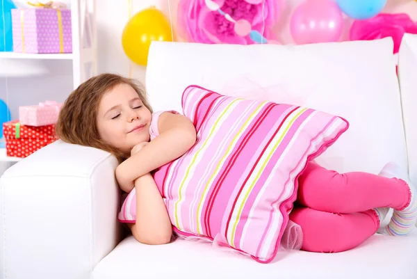 Pretty little girl slipping on sofa on celebratory background — Stock Photo, Image