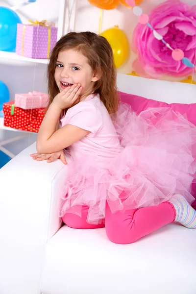 Hübsches kleines Mädchen sitzt auf Sofa auf festlichem Hintergrund — Stockfoto