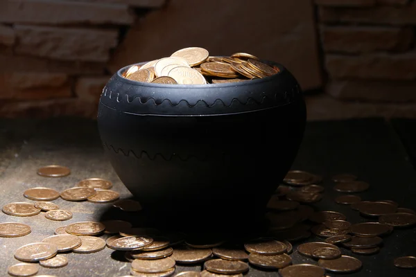 Golden coins in ceramic pot, on wooden table on dark background — Stock Photo, Image