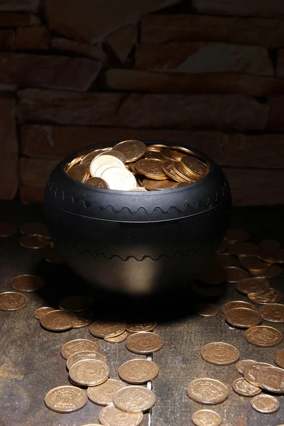 Golden coins in ceramic pot, on wooden table on dark background — Stock Photo, Image