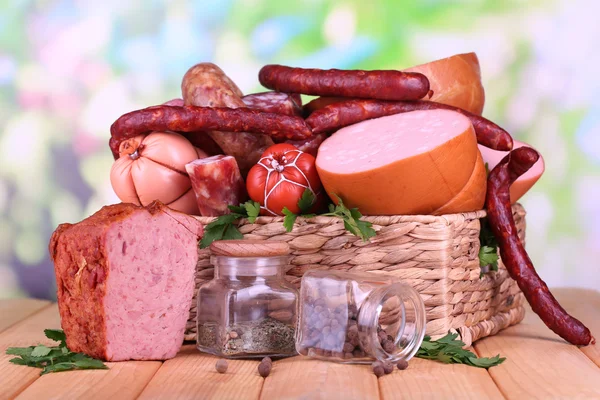 Lot of different sausages in basket on wooden table on natural background — Stock Photo, Image