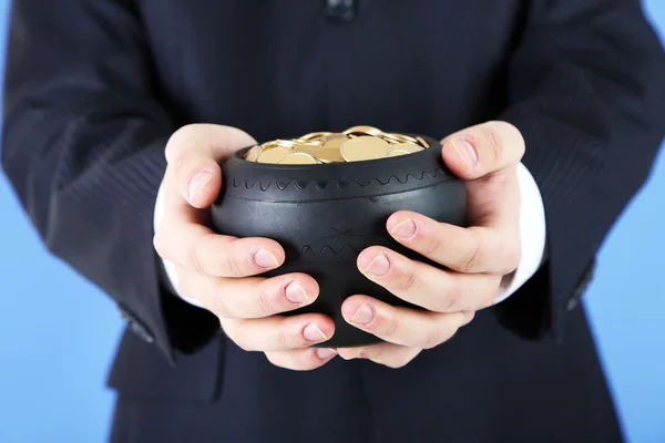 Maceta de cerámica con monedas de oro en manos masculinas, sobre fondo de color — Foto de Stock