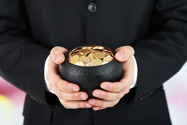 Keramiska potten med gyllene mynt i manliga händer, på ljus bakgrund — Stockfoto