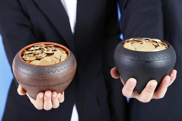 Две керамические горшки с золотыми монетами в мужских и женских руках, на цветном фоне — стоковое фото