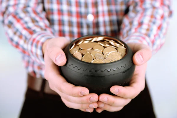 Keramische pot met gouden munten in mannelijke handen, op lichte achtergrond — Stockfoto