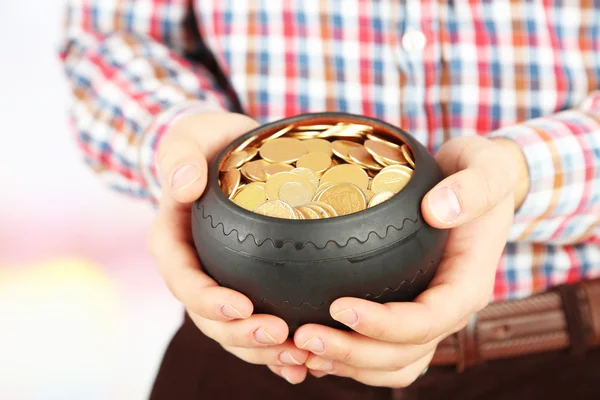 Keramiska potten med gyllene mynt i manliga händer, på ljus bakgrund — Stockfoto