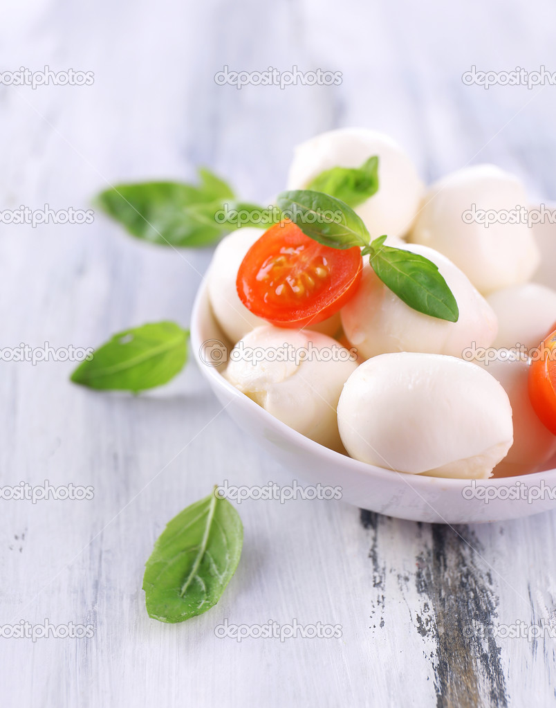 Tasty mozzarella cheese with basil and tomatoes in bowl, on wooden table