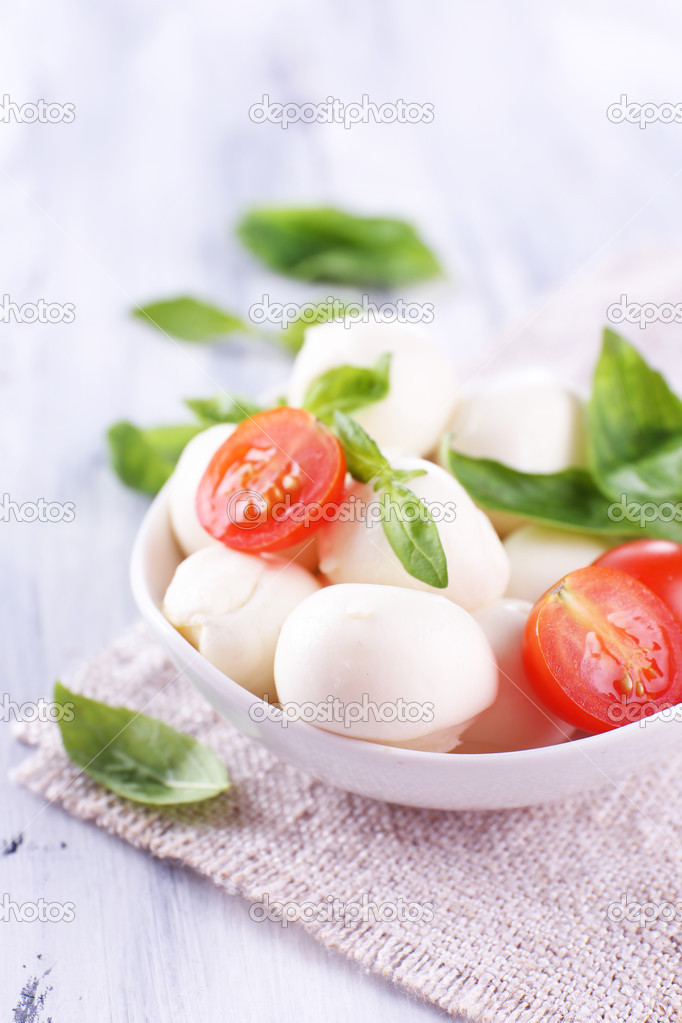 Tasty mozzarella cheese with basil and tomatoes in bowl, on wooden table