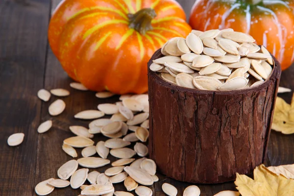 Semillas de calabaza en maceta con calabazas sobre fondo de madera — Foto de Stock