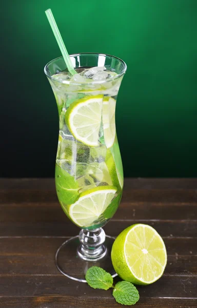 Cocktailglas mit Limette und Minze auf Tisch auf dunkelgrünem Hintergrund — Stockfoto