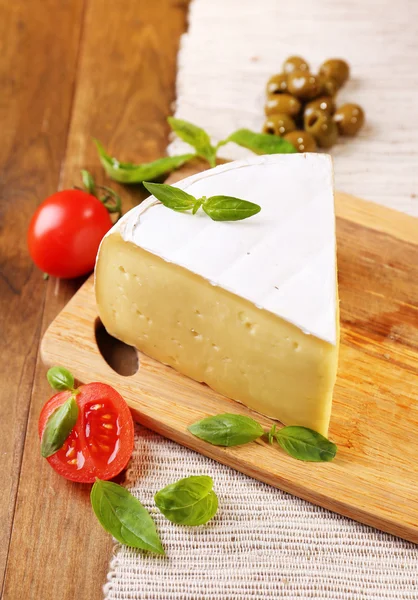 Chutný sýr camembert s rajčaty, olivami a bazalkou, na dřevěný stůl — Stock fotografie