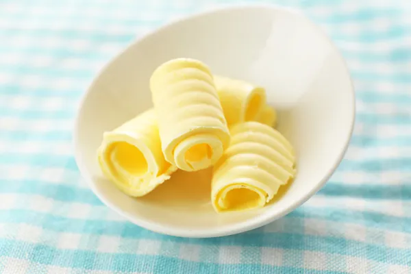 Curls of fresh butter in bowl, on blue tablecloth — Stock Photo, Image