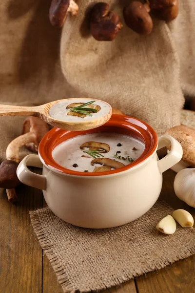 Mushroom soup in wooden spoon and pot, on wooden table, on sackcloth background — Stock Photo, Image