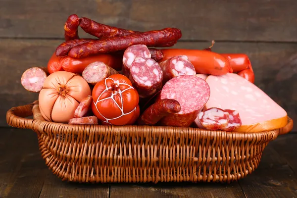 Lot of different sausages in basket on wooden table on wooden background — Stock Photo, Image