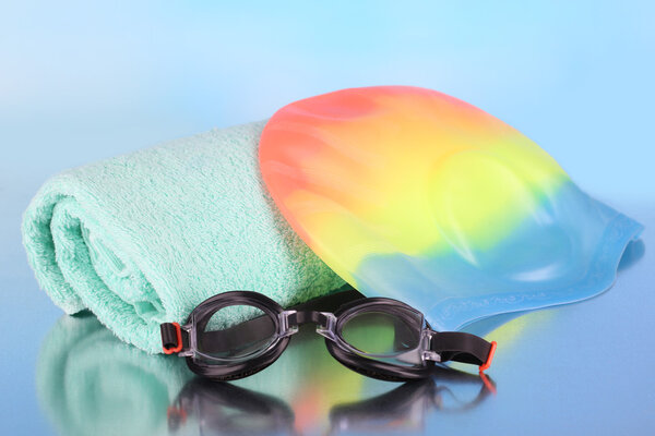 Set for pool: swim cap, goggles and towel on blue background