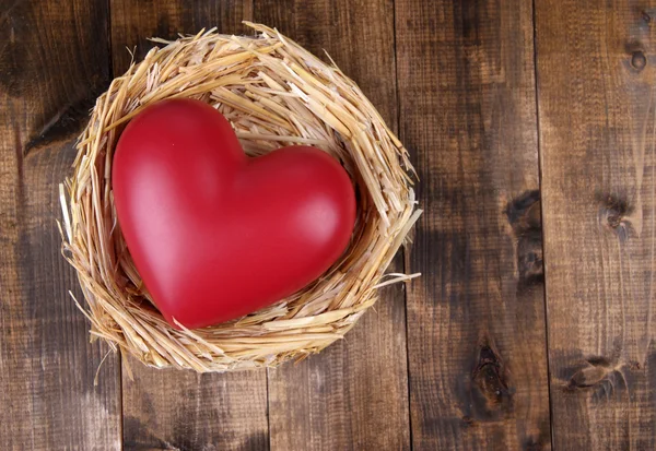 Decorative heart in nest, on wooden background — Stock Photo, Image