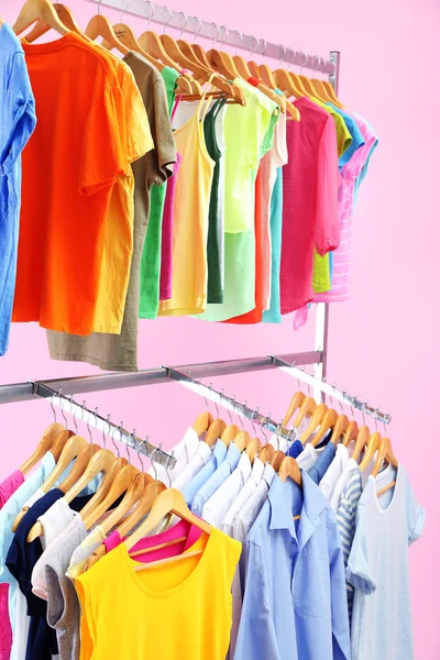 Different clothes on hangers, on pink background — Stock Photo, Image