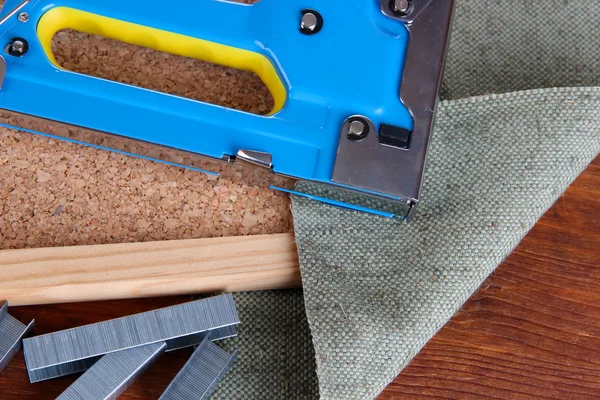 Строительный степлер со скобками и пробковой доской на деревянном фоне — стоковое фото