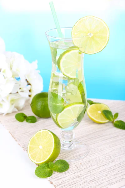 Glass of cocktail with lime and mint on table on light blue background — Stock Photo, Image