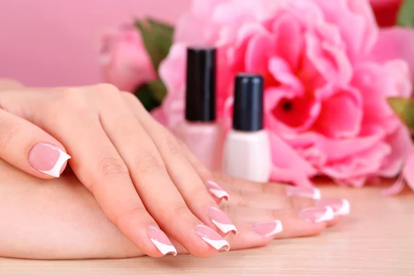 Beautiful woman hands with french manicure and flowers on wooden background — Stock Photo, Image