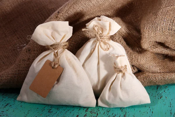 Sacks on color wooden table, on sackcloth background — Stock Photo, Image