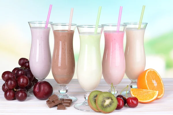 Batidos de leite com frutas na mesa no fundo azul claro — Fotografia de Stock