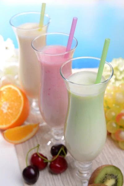 Milk shakes avec des fruits sur la table sur fond bleu clair — Photo