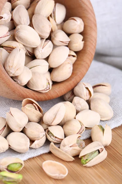 Pistachio nuts in wooden bowl on fabric background — Stock Photo, Image