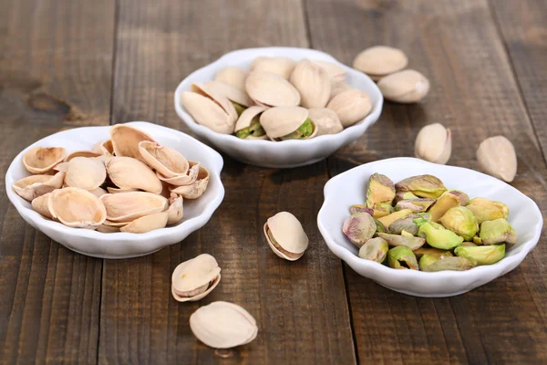 Pistachio nuts in small bowls on wooden background — Stock Photo, Image