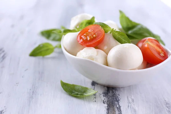 Tasty mozzarella cheese with basil and tomatoes in bowl, on wooden table — Stock Photo, Image