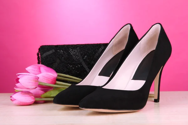 Beautiful black female shoes, bag and flowers on pink background — Stock Photo, Image