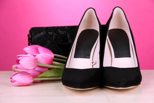 Piękne czarne kobiece buty, torby i kwiaty na różowym tle — Zdjęcie stockowe